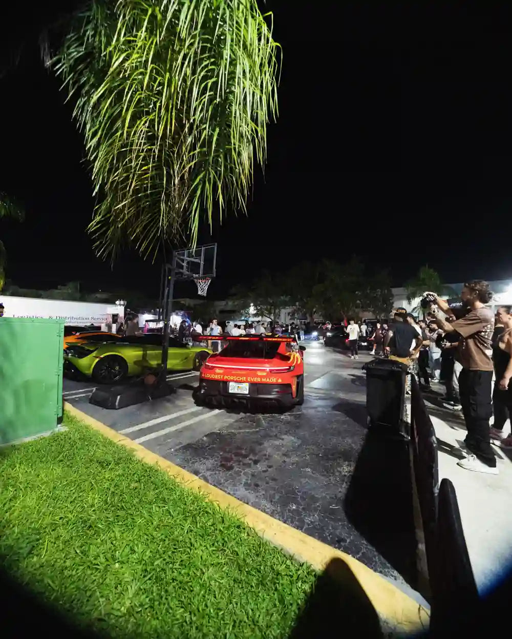 Cars and a nighttime crowd beneath the palms outside Ark